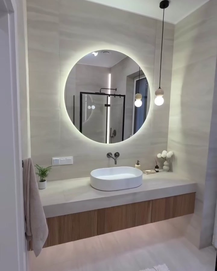 Bathroom with a round backlit mirror, vessel basin and fluted oak vanity