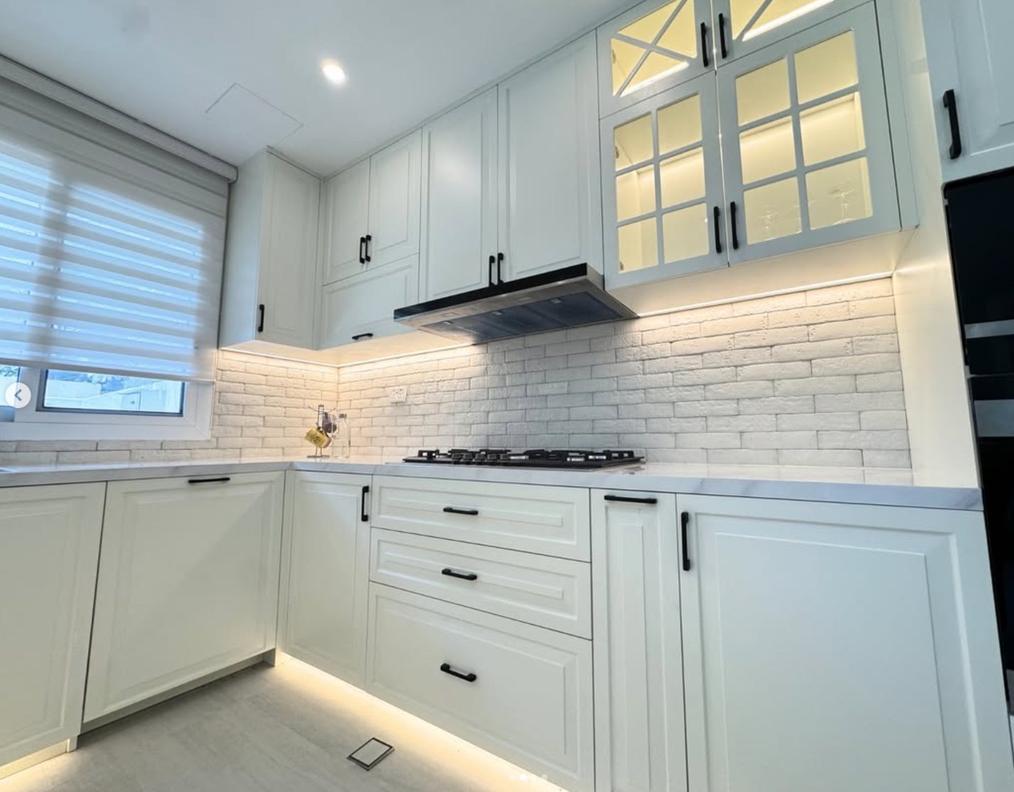 White shaker kitchen with glazed upper cabinets, brick backsplash and black handles