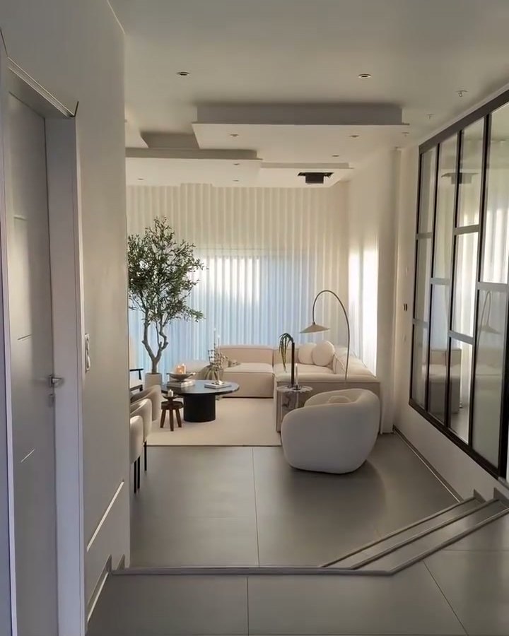 Living room with curved cream armchairs, an olive tree and sheer curtains