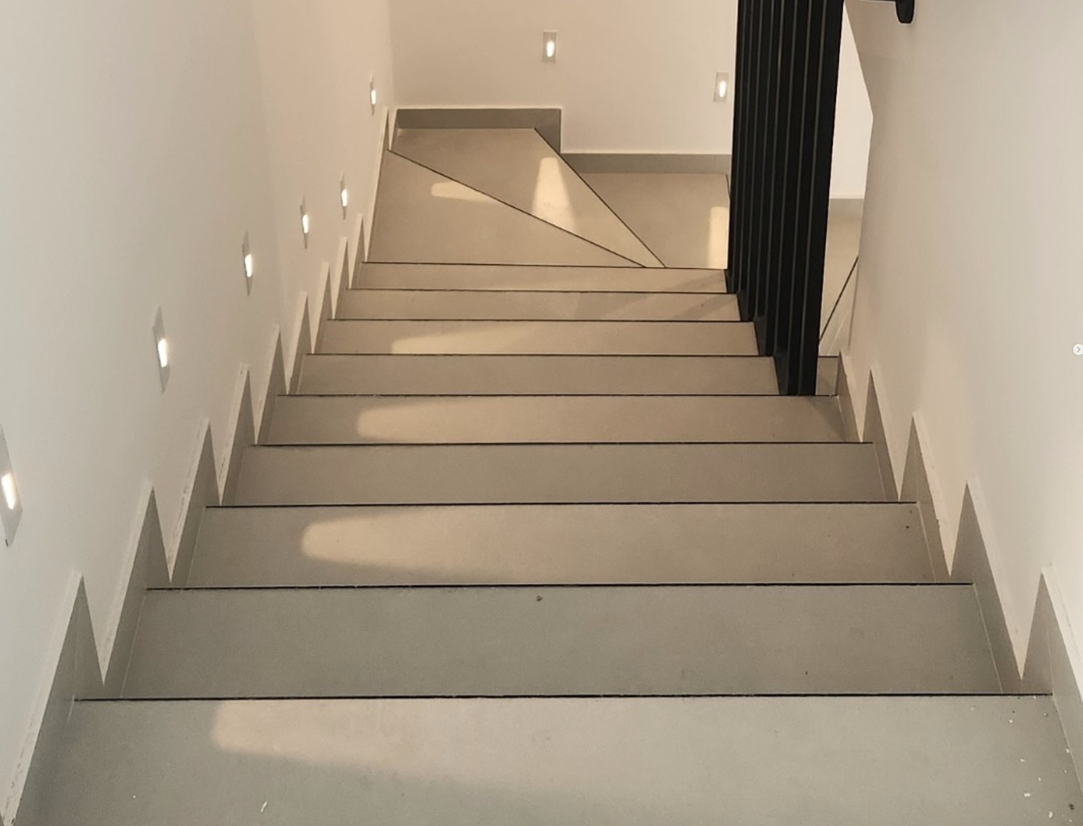 Villa staircase with porcelain treads, recessed wall lights and a black steel balustrade