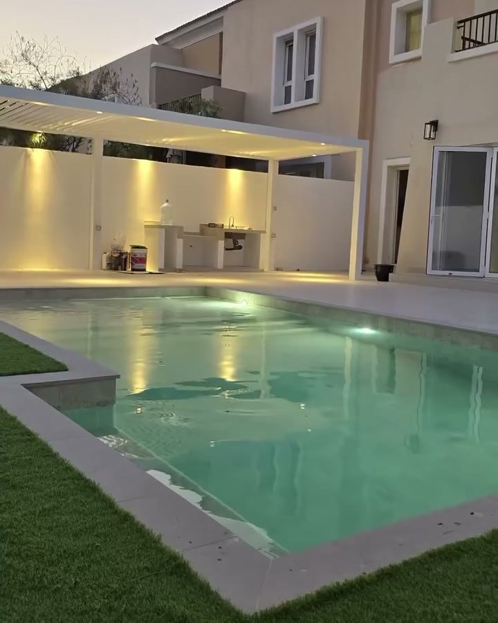 Villa garden at dusk with a lit swimming pool and a covered outdoor seating area